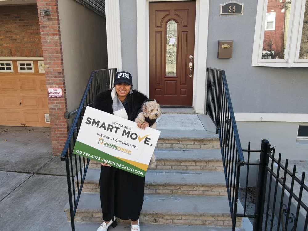 A HomeCheck client and her dog outside their newly inspected New Jersey home, holding a Smart Move sign
